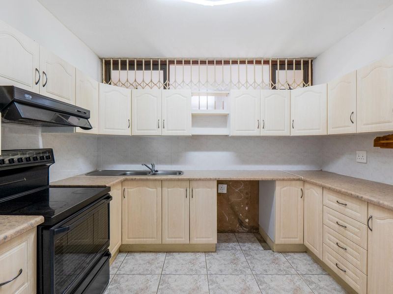 A functional kitchen featuring light-toned cabinetry, laminate countertops, a freestanding stove with extractor fan, and tiled flooring.
