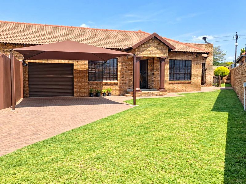 A well-maintained face brick house featuring a paved driveway, a shade sail carport, and a neat front lawn with secure boundary walls.
