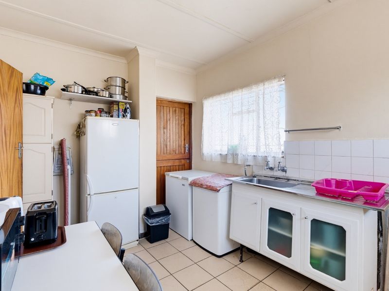 A functional kitchen area featuring tiled flooring, a stainless steel sink, built-in cabinetry, and a tiled splashback.