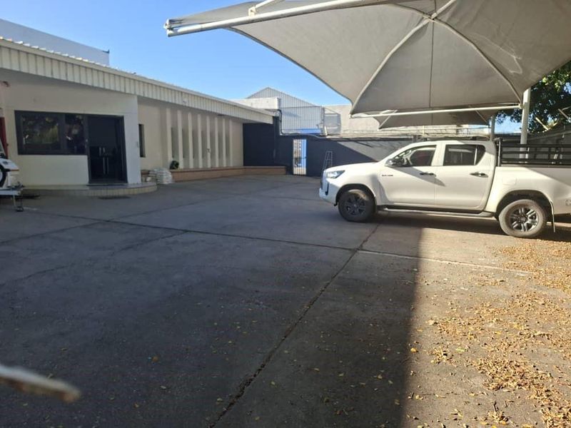 Rear exterior area featuring a large concrete paved yard, a shade sail structure, and access to the office building via a sliding glass door.