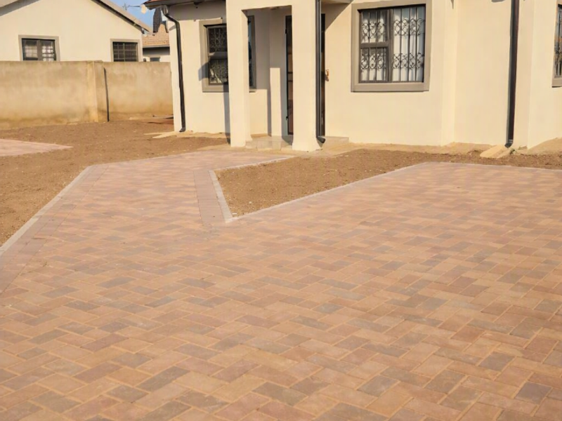Front view of a modern single-story house featuring a paved driveway, tiled roof, and security bars on the windows.