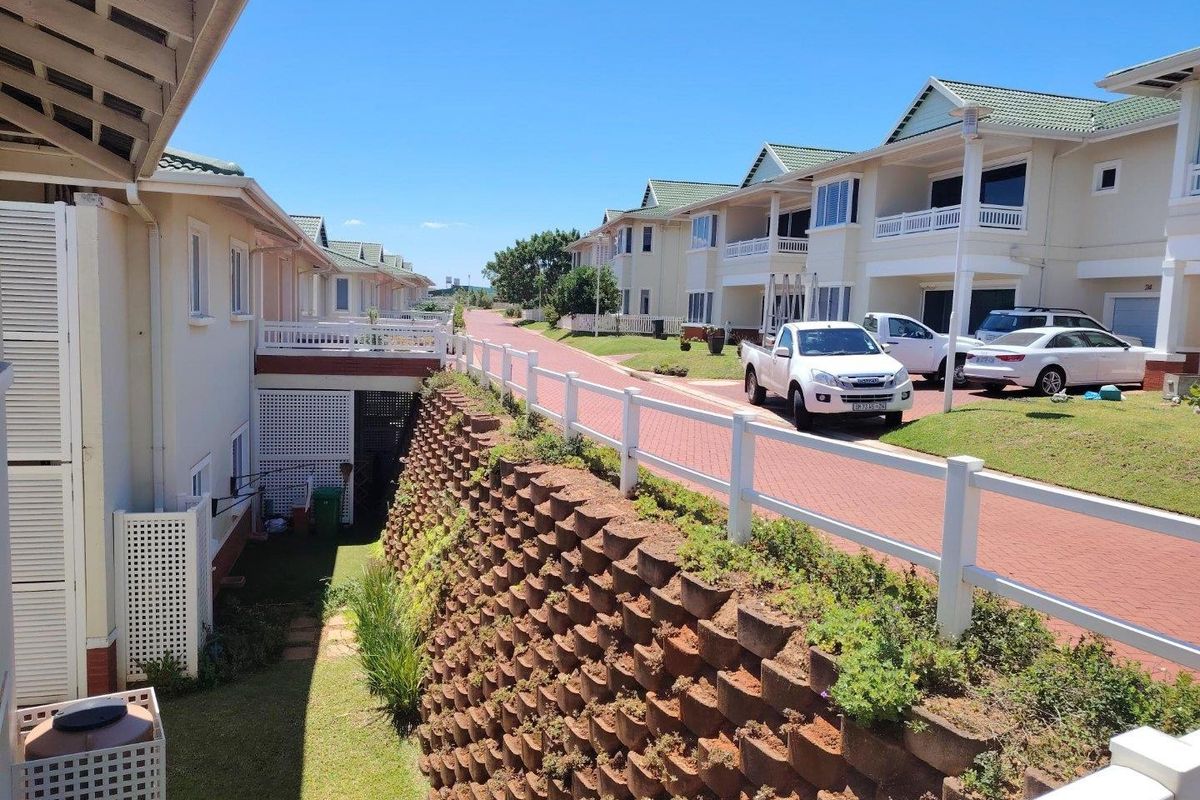 View of the apartment complex exterior featuring a tiered retaining wall, paved driveway, and private balcony access.