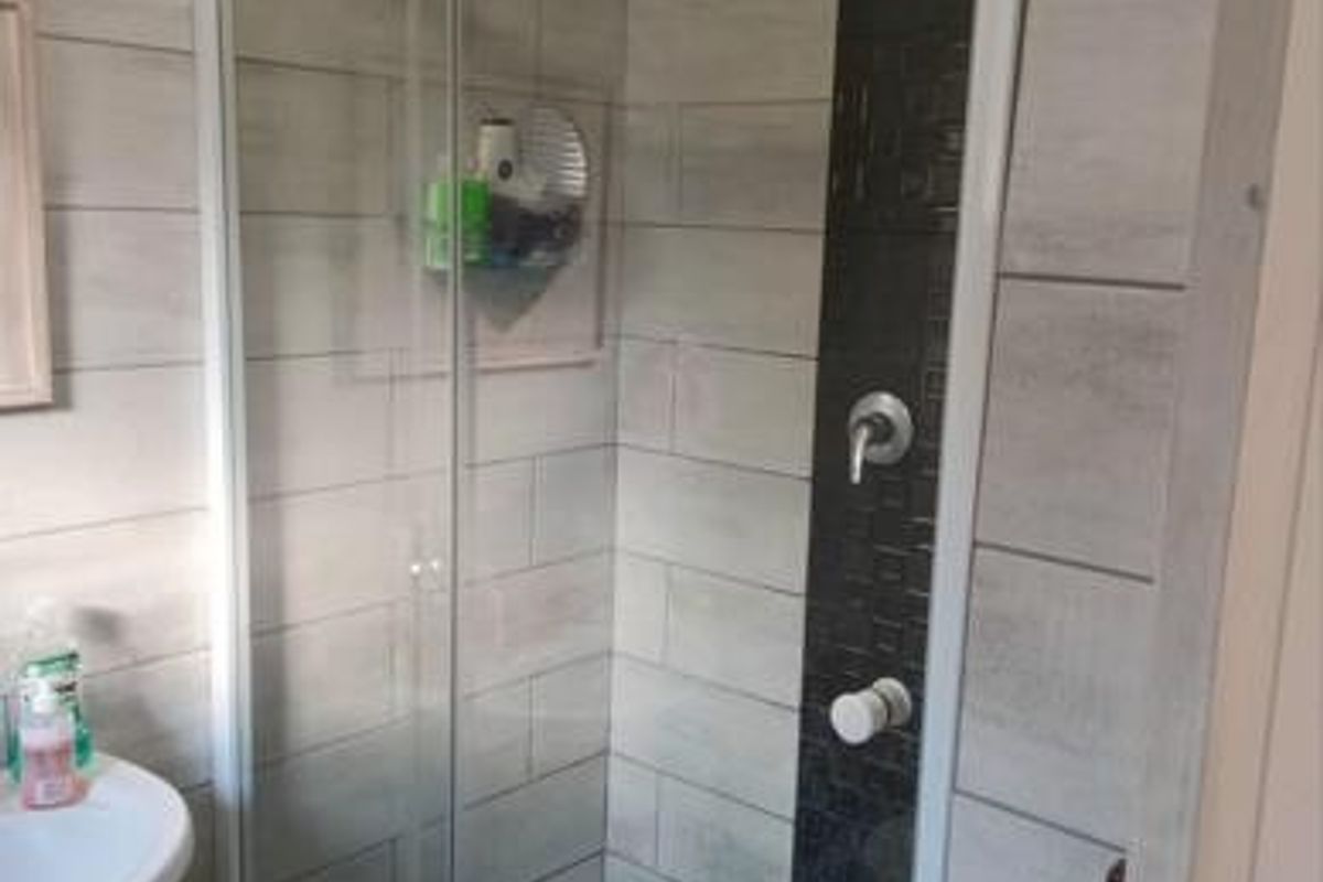 A functional bathroom featuring a glass-enclosed shower with modern tiled accents and a pedestal basin.
