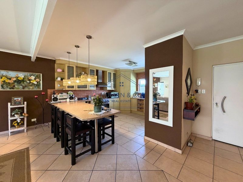 Open plan kitchen and living area featuring tiled flooring, extensive cabinetry, and a central breakfast bar with pendant lighting.