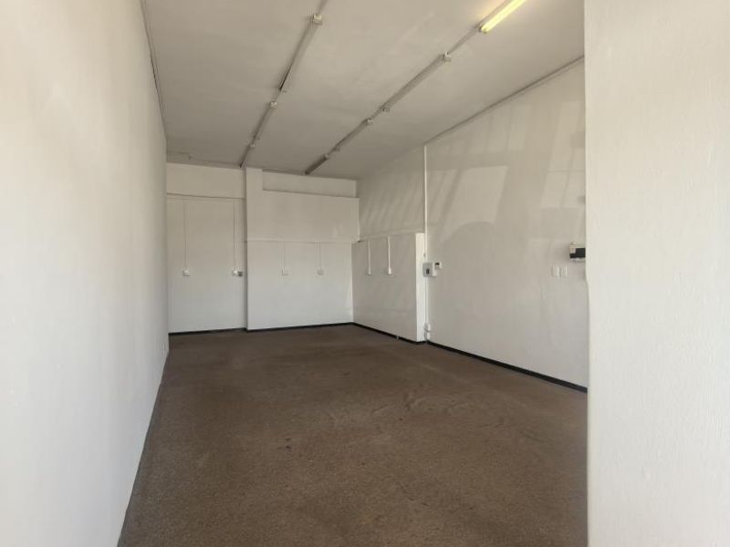 An empty, open-plan office space featuring carpeted flooring, fluorescent strip lighting, and built-in storage cupboards.