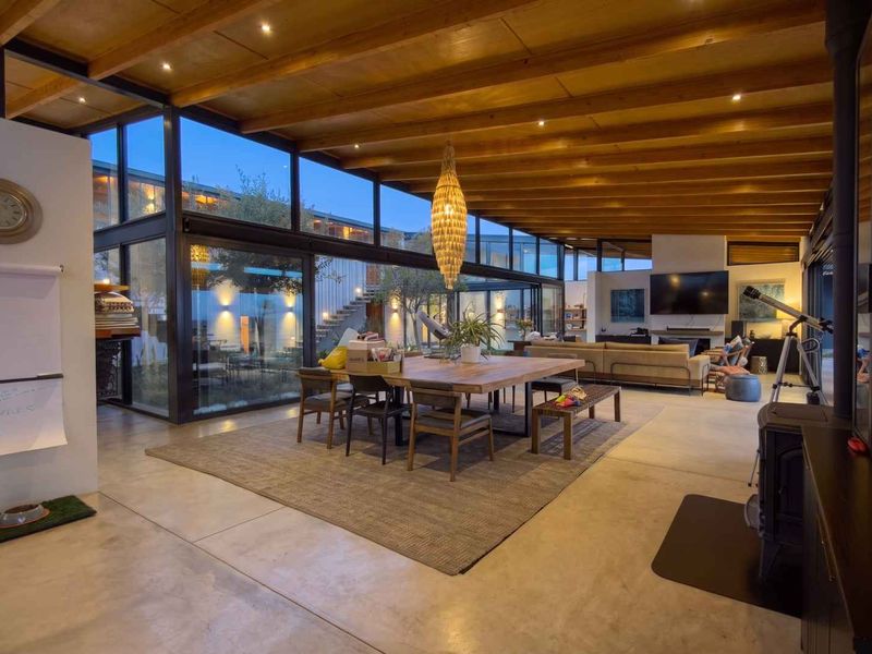 Spacious open-plan living area featuring polished concrete floors, exposed timber beam ceilings, and extensive floor-to-ceiling glass walls overlooking a central courtyard.
