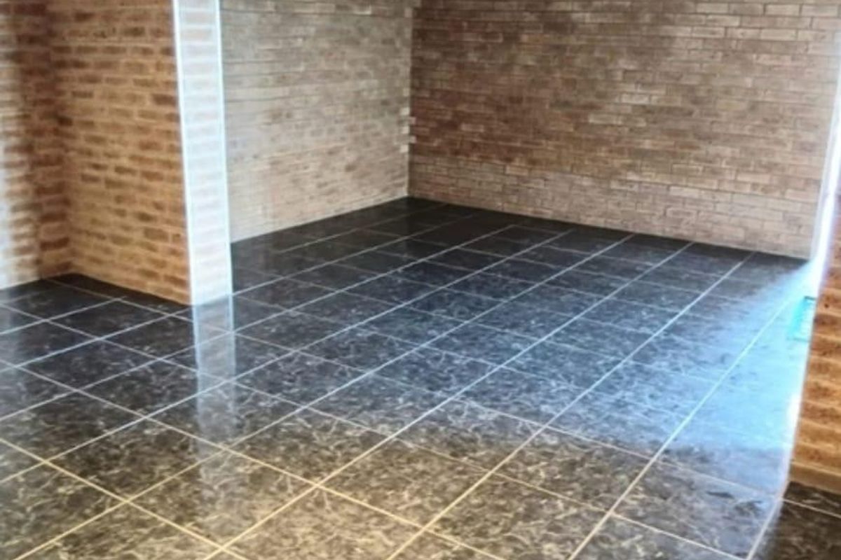 An empty living area featuring rustic exposed brick walls and polished dark marble-effect floor tiles.