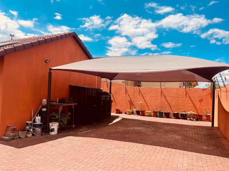 A paved rear outdoor area featuring a large shade sail structure, enclosed by high boundary walls and adjacent to the main house structure.