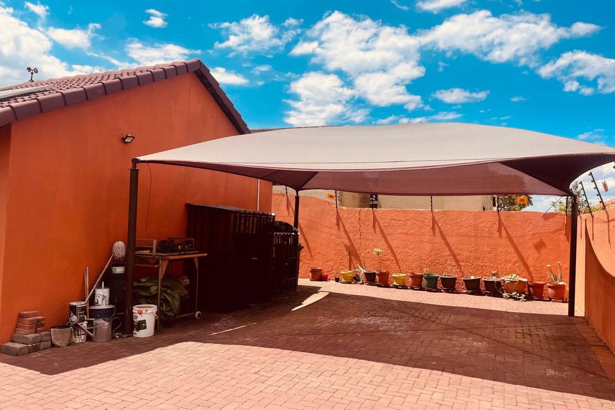 A paved rear outdoor area featuring a large shade sail structure, enclosed by high boundary walls and adjacent to the main house structure.