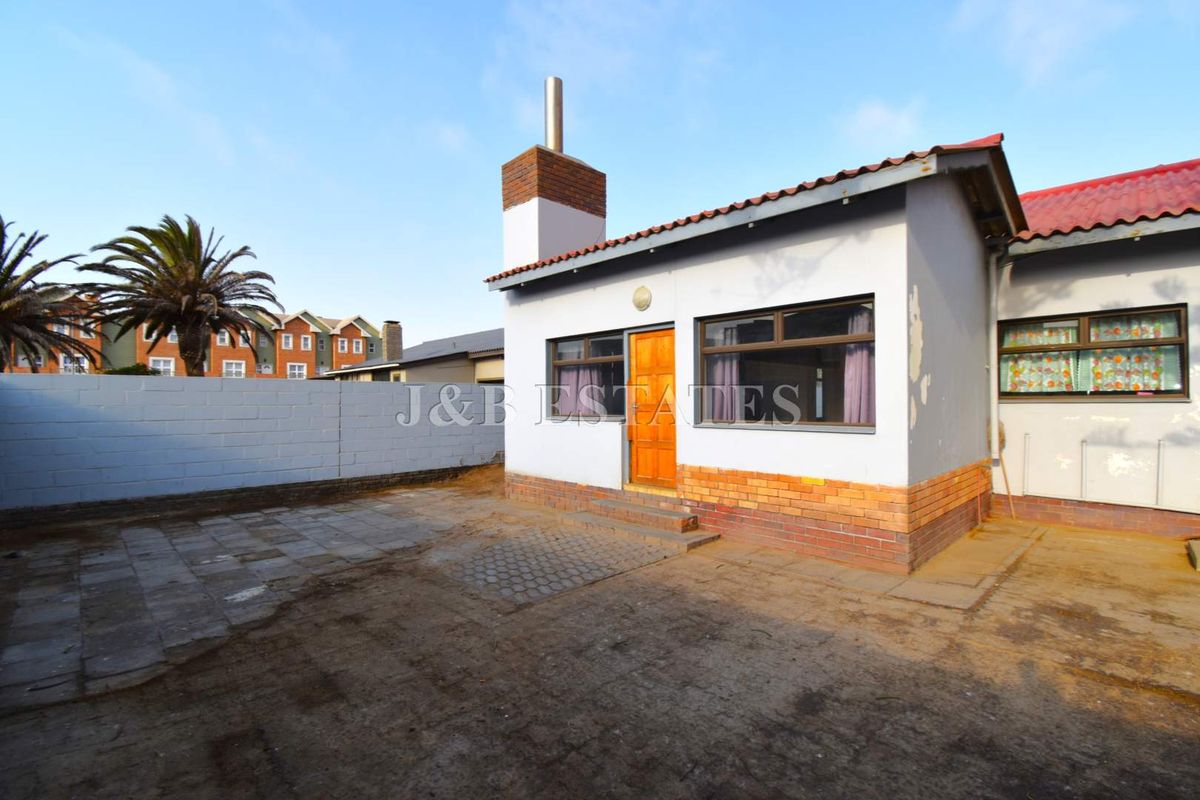 Rear view of the property featuring a paved patio area, brick chimney stack, and exterior wall finishes requiring maintenance.