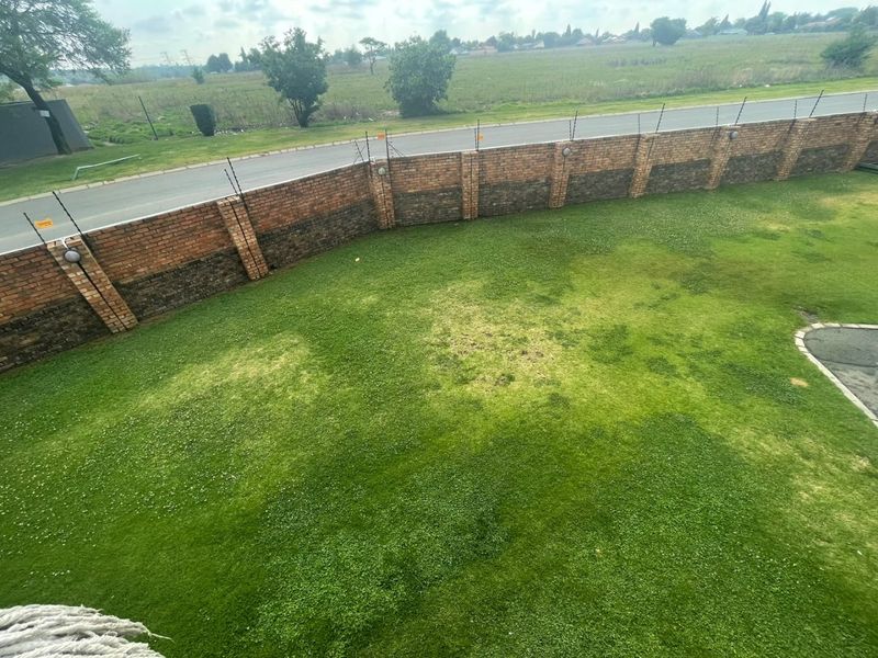 An elevated view of a private garden featuring a lawn enclosed by a brick boundary wall with integrated electric fencing.