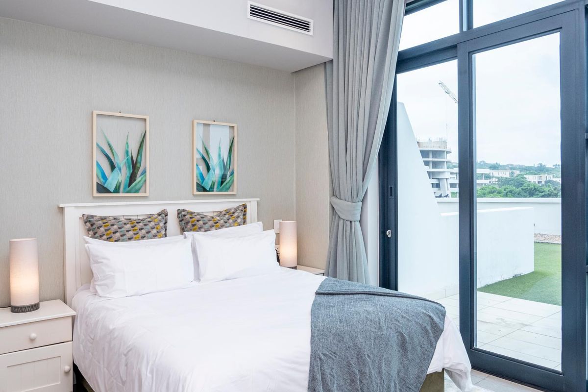 Modern bedroom featuring ducted air conditioning and a large sliding glass door providing direct access to a private balcony.