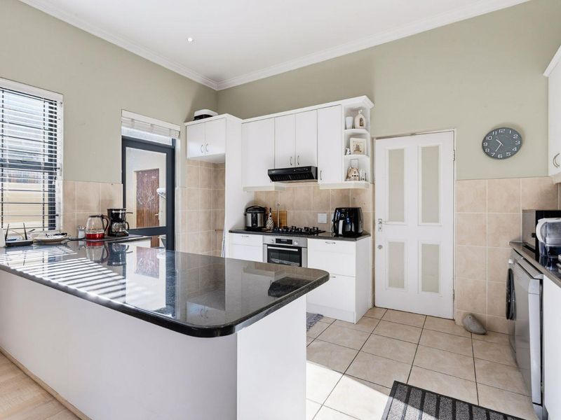 A functional kitchen featuring white cabinetry, granite countertops, a gas hob with extractor, and tiled flooring with direct access to the exterior.