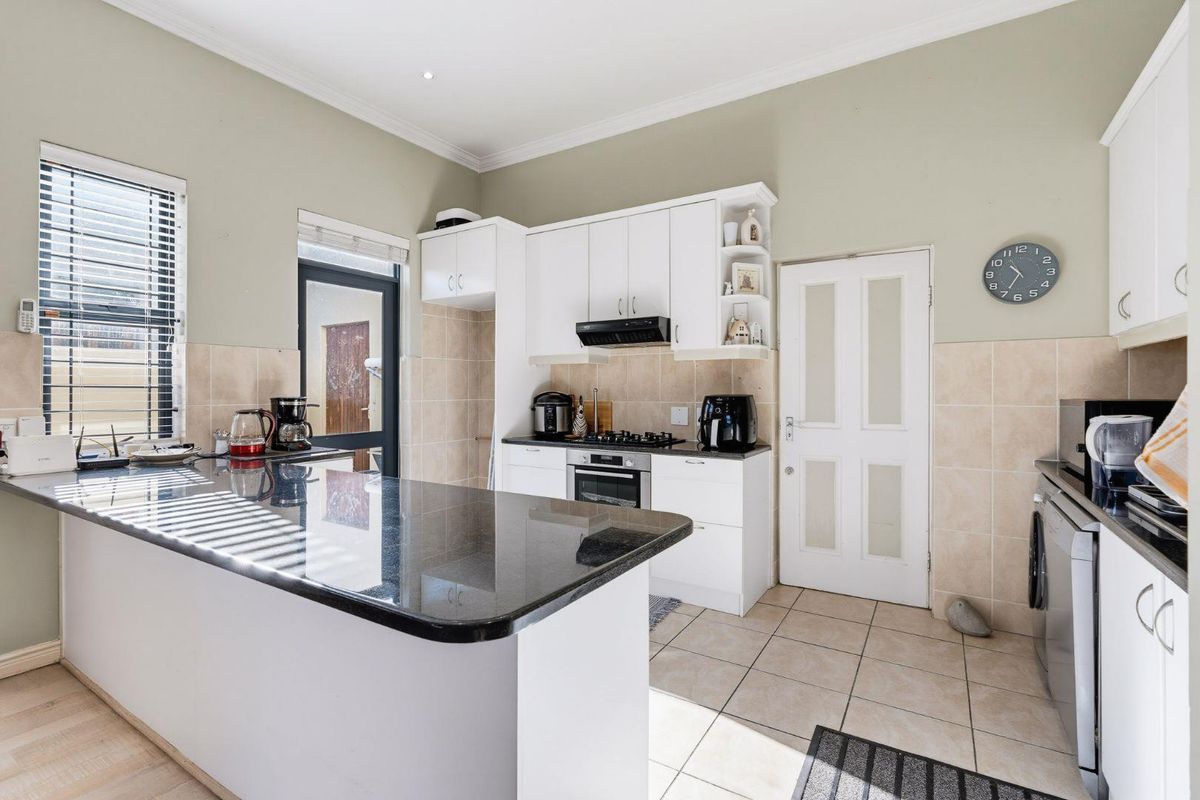 A functional kitchen featuring white cabinetry, granite countertops, a gas hob with extractor, and tiled flooring with direct access to the exterior.