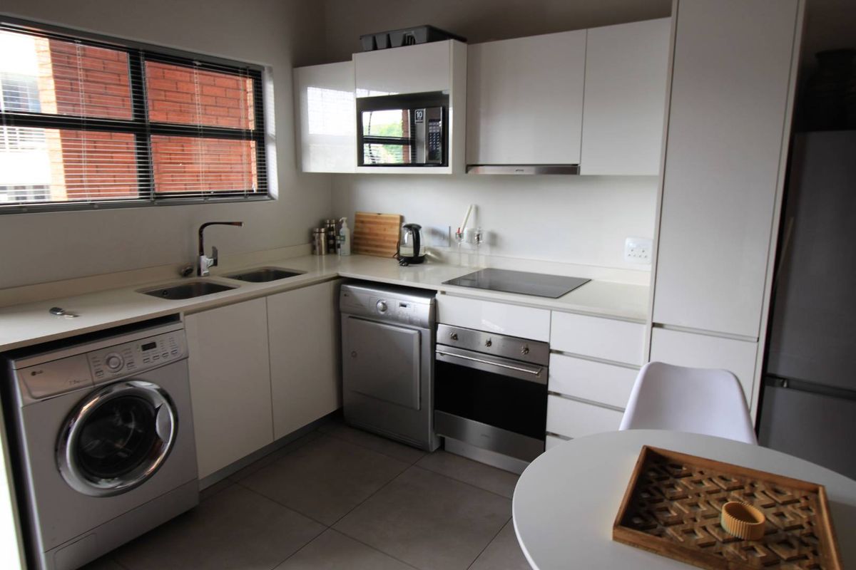 Modern kitchen featuring sleek white cabinetry, stone countertops, integrated appliances including an oven, hob, and extractor fan, with tiled flooring and ample natural light.