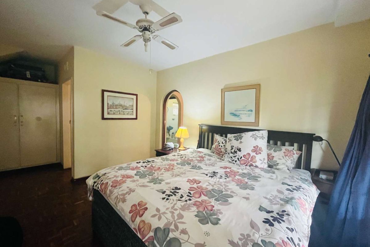 A bedroom featuring parquet flooring, a ceiling fan, and a built-in wardrobe, offering a functional and comfortable living space.