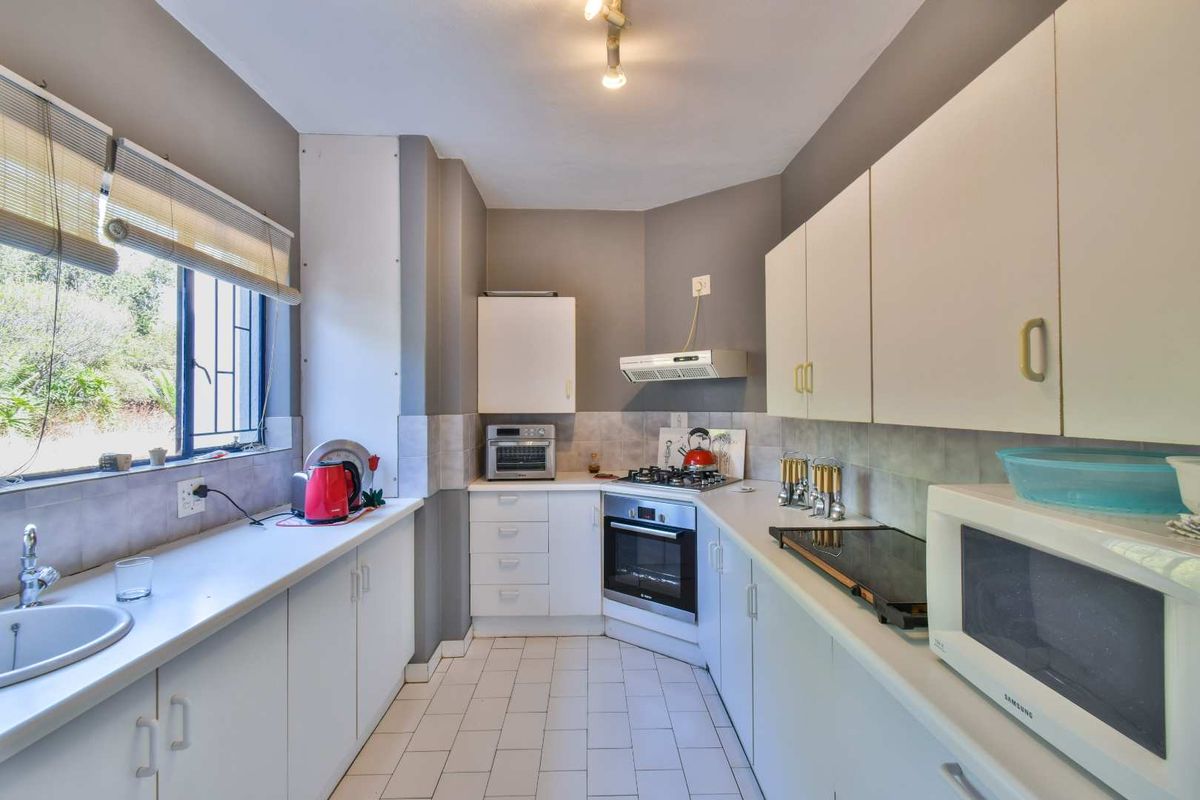 A functional galley-style kitchen featuring white cabinetry, tiled flooring, a built-in oven, gas hob, and an extractor fan.