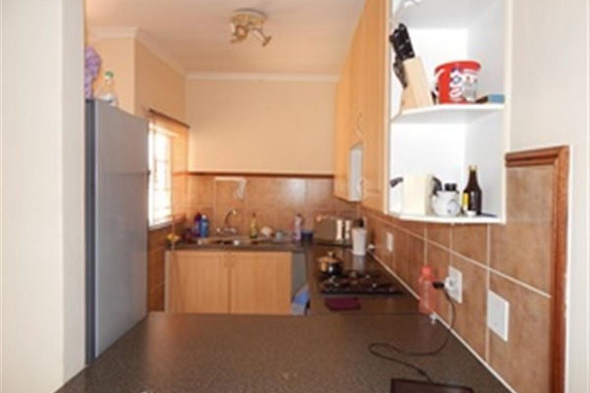A functional kitchen featuring light wood cabinetry, dark laminate countertops, a built-in hob, and a tiled splashback, offering a practical layout for daily use.