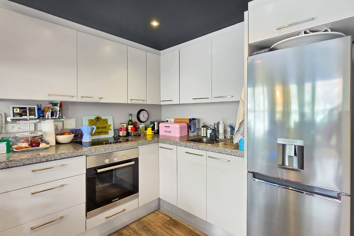 Modern kitchen featuring white cabinetry, granite countertops, built-in oven, electric hob, and recessed lighting with a contrasting dark ceiling.