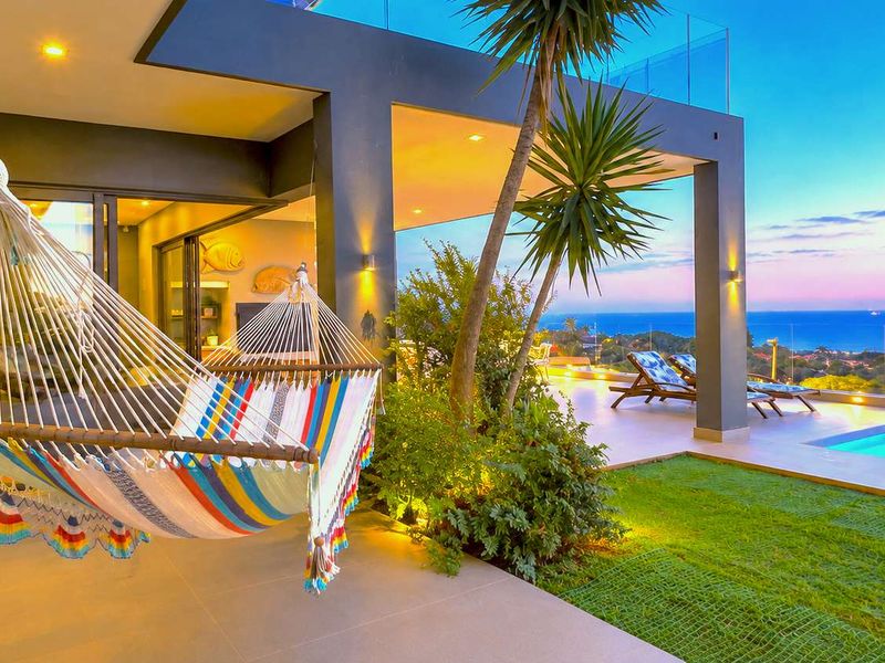 A modern covered patio featuring tiled flooring and recessed lighting, seamlessly connecting to a swimming pool area with expansive coastal views.