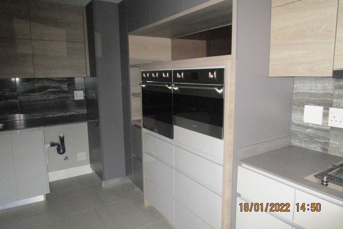 Modern kitchen featuring sleek grey cabinetry, stone countertops, a built-in double oven, and a gas hob with tiled flooring.