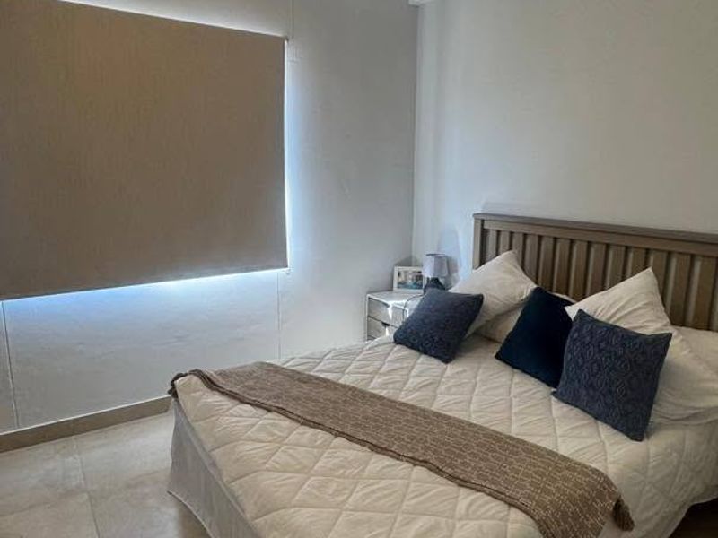 A bedroom featuring neutral tiled flooring, a roller blind for privacy, and a central ceiling light fixture.