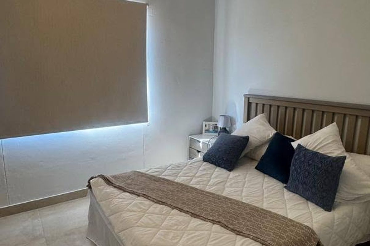 A bedroom featuring neutral tiled flooring, a roller blind for privacy, and a central ceiling light fixture.