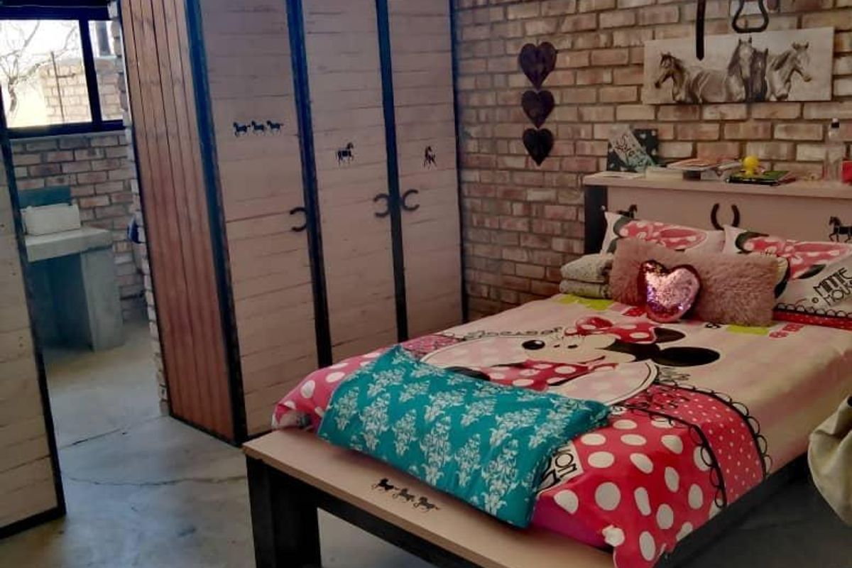 A rustic bedroom featuring exposed brick walls, industrial-style metal window frames, and a high corrugated metal ceiling, creating a unique farm-style aesthetic.