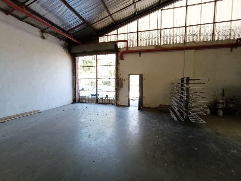 Spacious industrial utility area featuring high-pitched roofing, exposed fire suppression piping, concrete flooring, and a large roller shutter door for vehicle access.