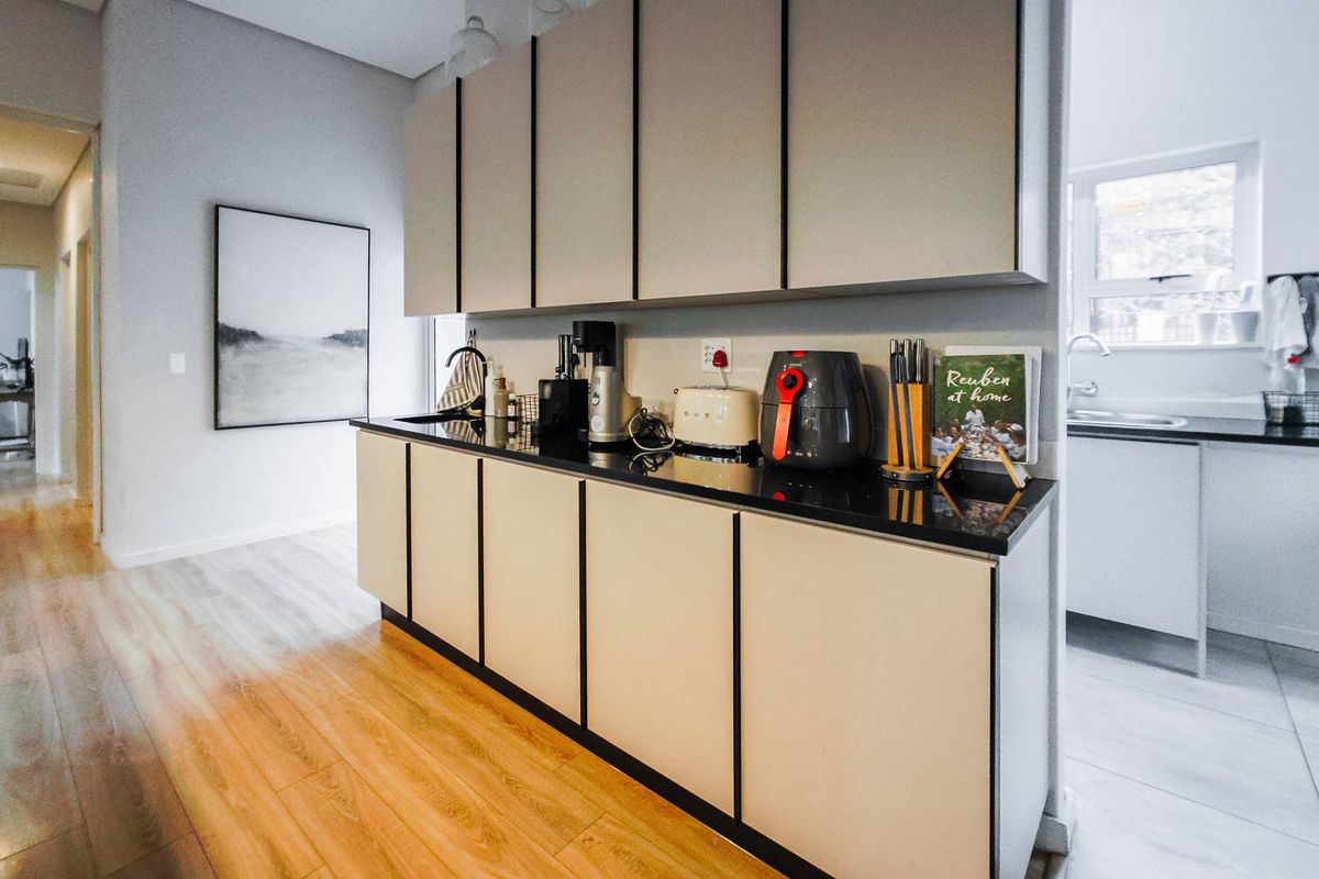 A modern kitchen featuring sleek cabinetry, dark stone countertops, and integrated sink, with a clean, contemporary aesthetic and wood-look flooring.