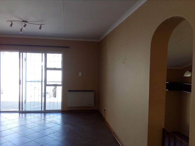 Spacious living area featuring tiled flooring, a wall-mounted heater, and a sliding glass door providing access to the exterior.
