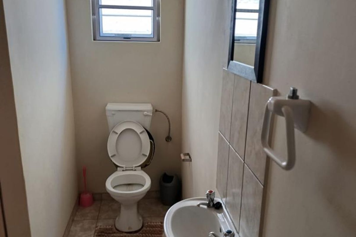 A compact guest bathroom featuring a standard toilet, wall-mounted basin with tiled splashback, and tiled flooring.