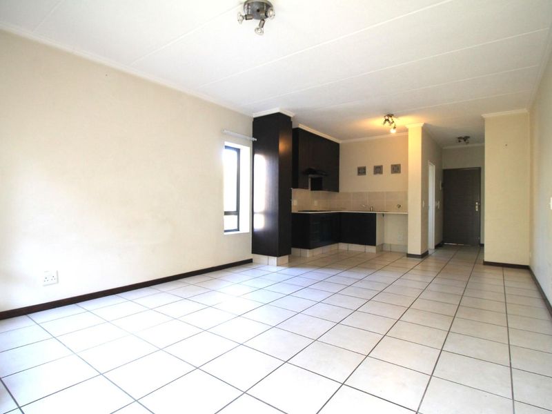 An open-plan living and kitchen area featuring neutral tiled flooring, dark built-in kitchen cabinetry, and a functional layout.