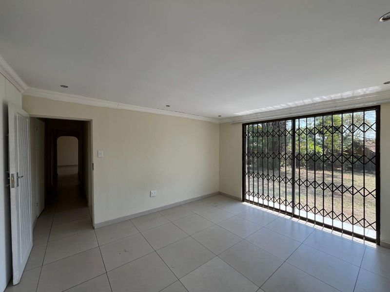 A bright, empty living room featuring neutral tiled flooring, recessed lighting, and a large sliding glass door with a security gate leading outdoors.
