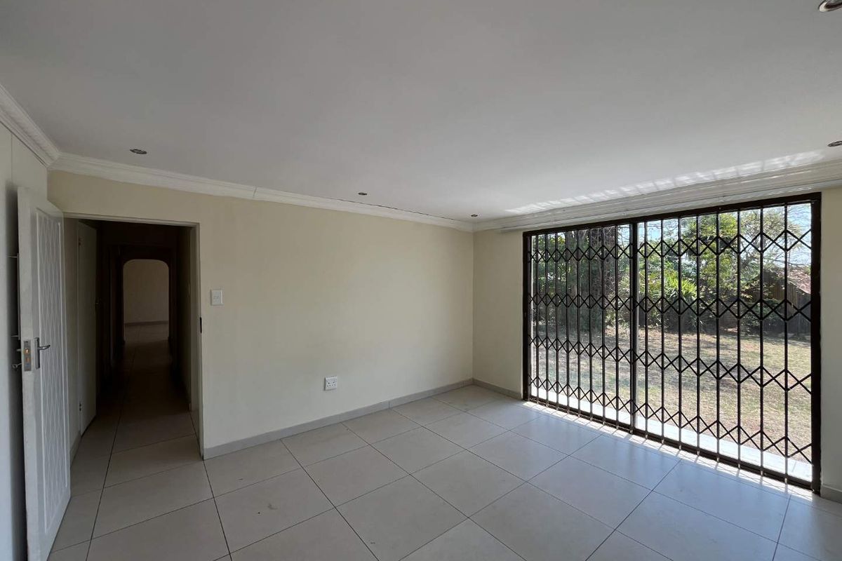 A bright, empty living room featuring neutral tiled flooring, recessed lighting, and a large sliding glass door with a security gate leading outdoors.