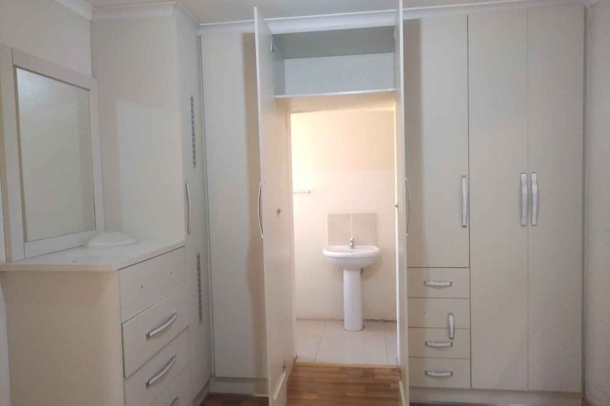 Bedroom featuring extensive built-in cupboards and an en-suite area with a pedestal basin and laminate flooring.