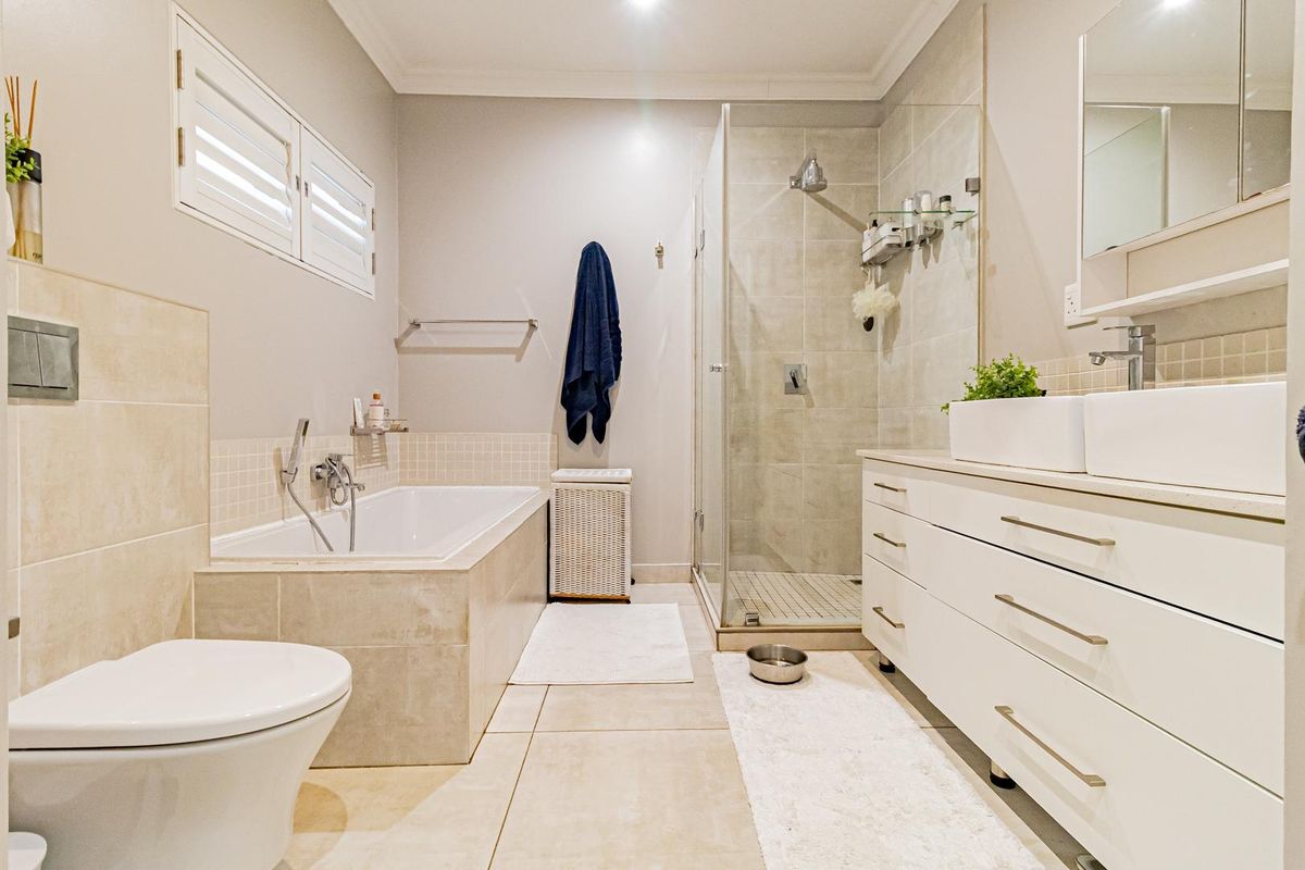 Modern bathroom featuring a tiled bathtub, glass-enclosed shower, dual vanity with storage, and a wall-mounted toilet.