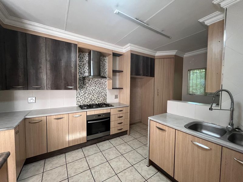 A functional kitchen featuring wood-look cabinetry, a gas hob with extractor fan, mosaic splashback, and tiled flooring.