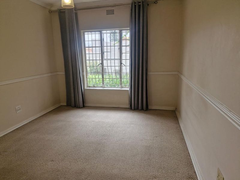A vacant bedroom featuring carpeted flooring, chair rail molding, and a window fitted with security bars.