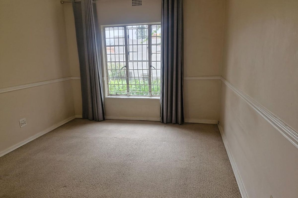 A vacant bedroom featuring carpeted flooring, chair rail molding, and a window fitted with security bars.