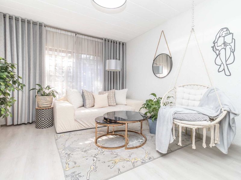 A bright and modern living room featuring light-toned laminate flooring, neutral walls, and large windows dressed with floor-to-ceiling curtains.