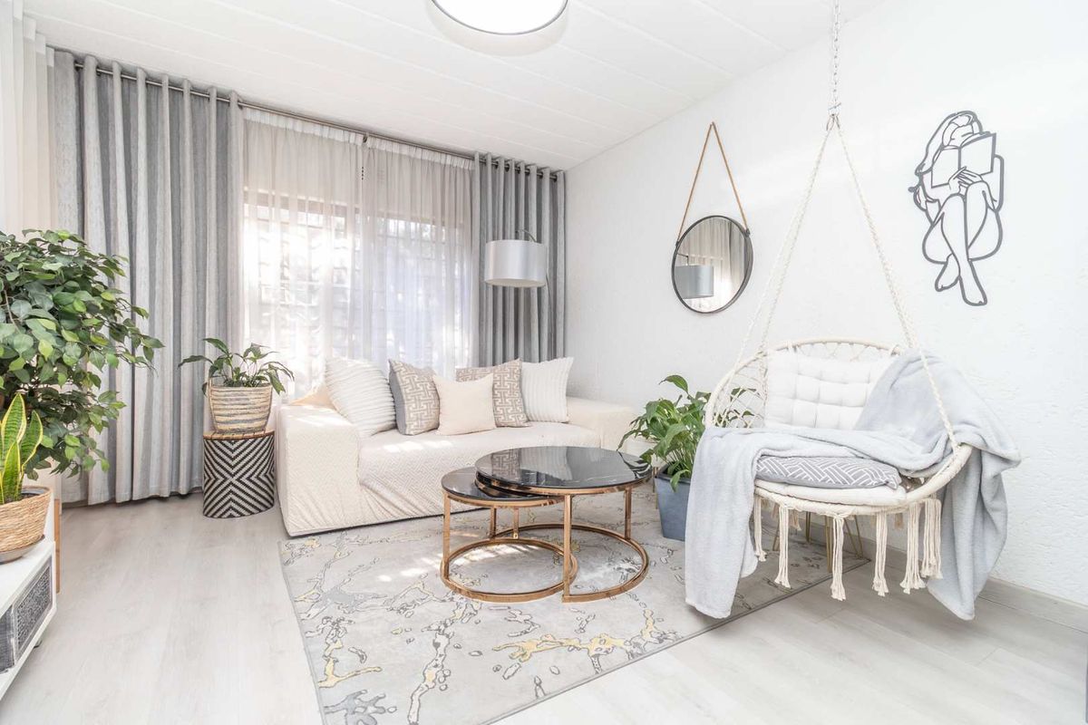 A bright and modern living room featuring light-toned laminate flooring, neutral walls, and large windows dressed with floor-to-ceiling curtains.