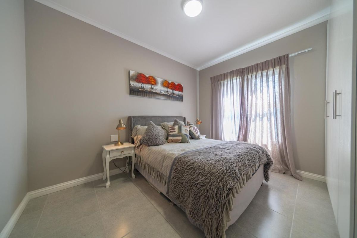 A well-maintained bedroom featuring neutral wall tones, tiled flooring, built-in cupboards, and large windows with curtain tracks.