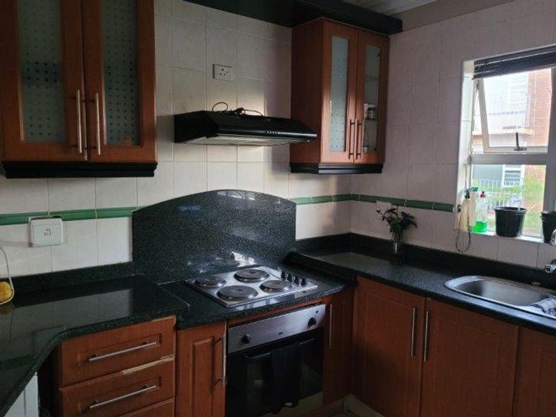 A functional kitchen featuring wooden cabinetry, granite countertops, a built-in oven, electric hob, and an extractor fan with a tiled backsplash.
