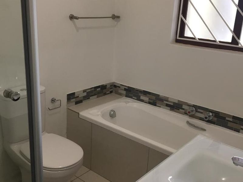 A clean, functional bathroom featuring a built-in bathtub, vanity basin, toilet, and tiled finishes with a mosaic accent border.