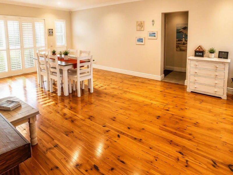 Spacious open-plan living and dining area featuring polished timber flooring, crown molding, and classic french doors with plantation shutters.