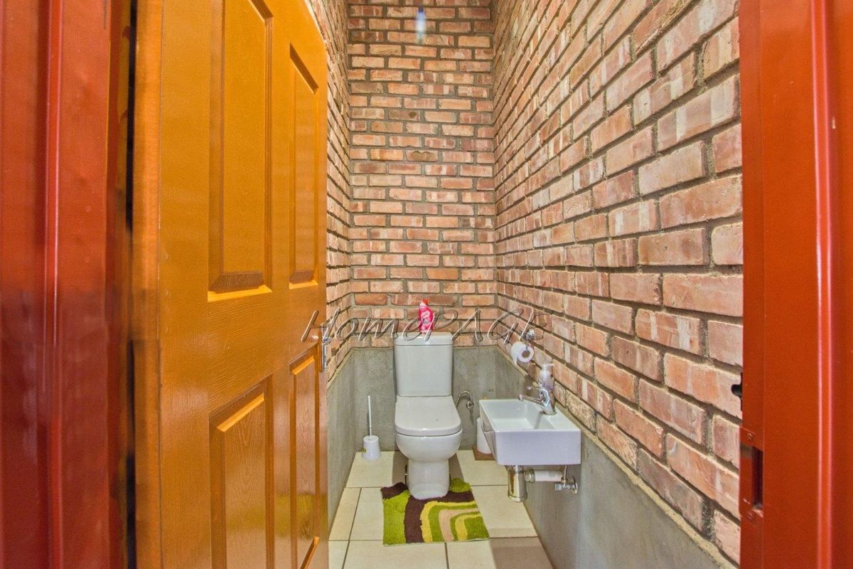 A compact guest bathroom featuring exposed brick walls, a wall-mounted basin, and a standard toilet suite.