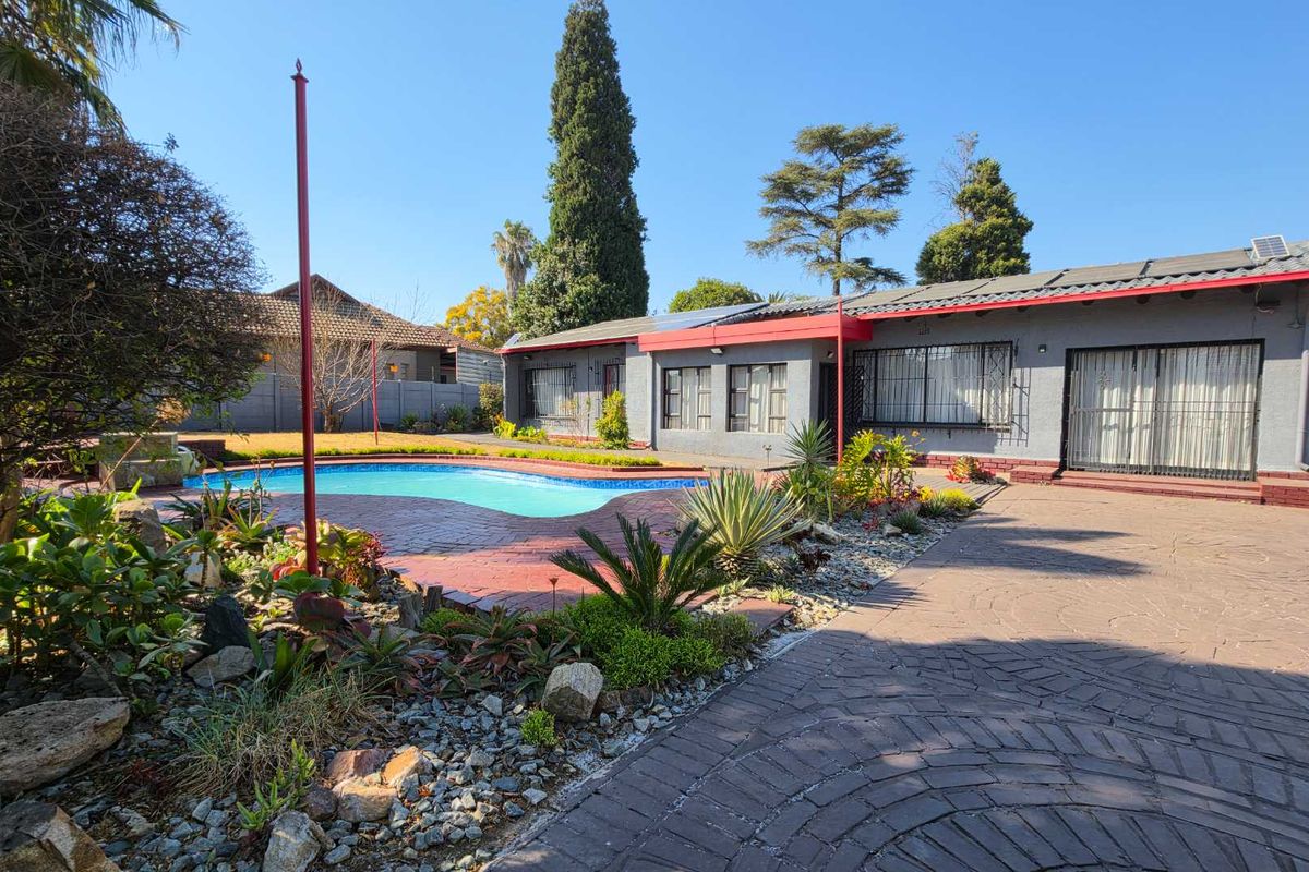 Rear exterior view featuring a swimming pool, brick paved patio area, and established garden with solar panels installed on the roof.