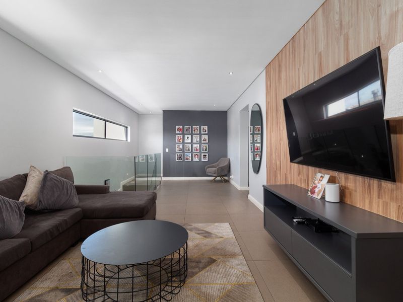 Modern living room featuring a wood veneer feature wall, glass balustrade, and sleek tiled flooring with recessed lighting.