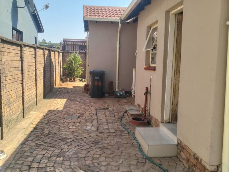 A side exterior area featuring brick paving, a boundary wall, and external plumbing fixtures along the side of the house.
